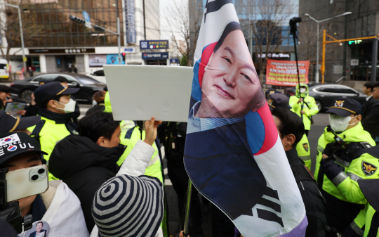 내란 우두머리 혐의로 기소된 윤석열 전 대통령의 첫 형사재판이 열린 14일 서울 서초구 서울중앙지방법원 앞에서 한 지지자가 윤 전 대통령 얼굴이 새겨진 태극기를 들고 서 있다.  <연합뉴스>